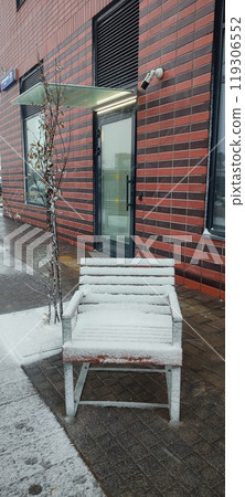 Snow-covered chair outside a modern building on a chilly winter day in an urban setting Snow-covered chair outside a modern building on a chilly winter day in an urban setting 119306552