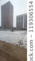 Snowfall blankets urban landscape outside residential buildings during winter morning 119306554