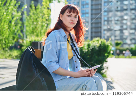 Young female college student with backpack using smartphone, outdoors 119306744