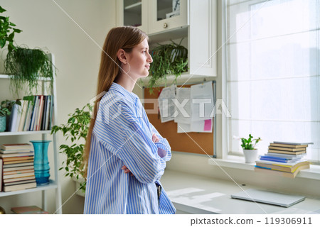 Smiling confident young woman looking out the window, in home interior 119306911