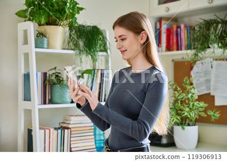 Happy female teenager using smartphone, standing at home Happy female teenager using smartphone, standing at home 119306913