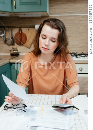 woman pays bills online, sits in kitchen with receipts and calculator. Online banking woman pays bills online, sits in kitchen with receipts and calculator. Online banking 119307132