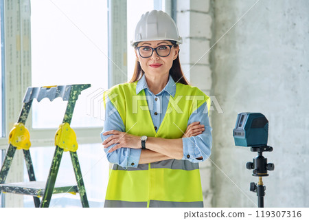 Woman in safety vest hard hat with crossed arms on new residential or commercial real estate site 119307316