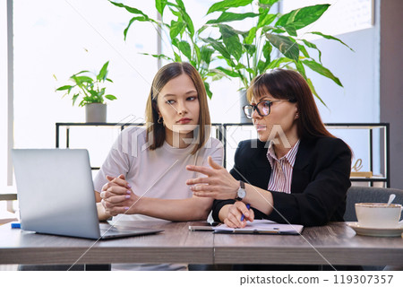 Two women sitting at table in coworking space with laptop Two women sitting at table in coworking space with laptop 119307357