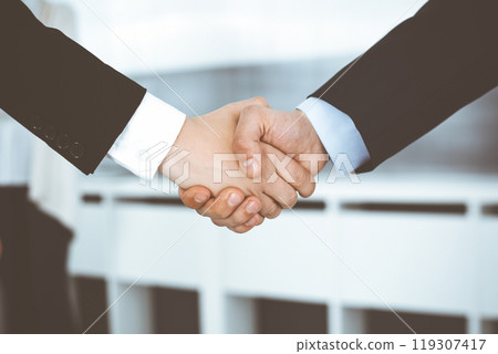 Businessman and woman shaking hands with colleagues at the background. Handshake at meeting in office. Concept of success in business Businessman and woman shaking hands with colleagues at the background. Handshake at meeting in office. Concept of success in business 119307417