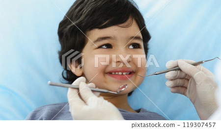 Cute arab boy sitting at dental chair with open mouth during oral checking up with doctor. Visiting dentist office. Stomatology concept Cute arab boy sitting at dental chair with open mouth during oral checking up with doctor. Visiting dentist office. Stomatology concept 119307457