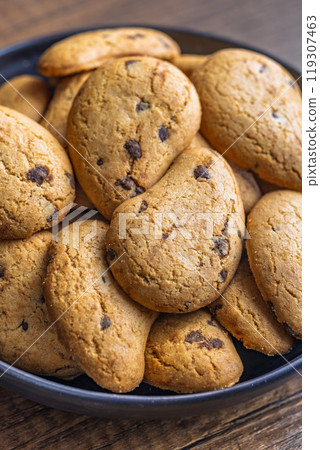 Biscotti frollini con gocce di cioccolato. Chocolate cookies on plate on wooden table. 119307463