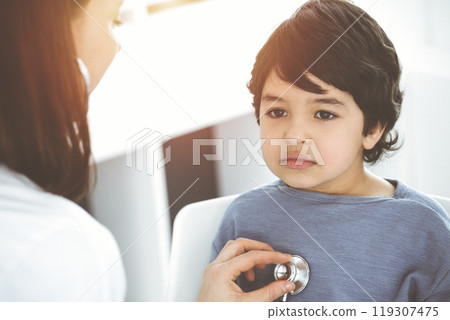 Doctor-woman examining a child patient by stethoscope in sunny clinik. Medicine concept 119307475