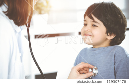 Doctor-woman examining a child patient by stethoscope in sunny clinik. Medicine concept Doctor-woman examining a child patient by stethoscope in sunny clinik. Medicine concept 119307476