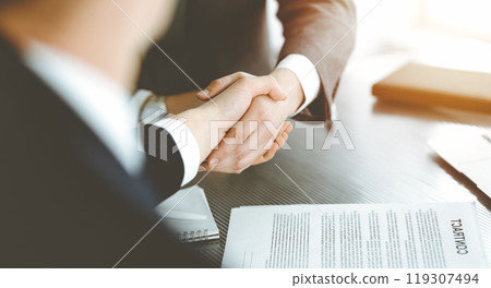 Unknown businessman shaking hands with his colleague or partner above the desk in sunny office, close-up Unknown businessman shaking hands with his colleague or partner above the desk in sunny office, close-up 119307494
