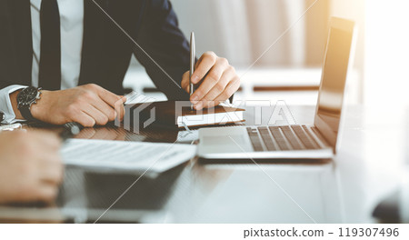 Unknown businessmen and woman sitting, working and discussing questions at meeting in sunny office, close-up. Success concept Unknown businessmen and woman sitting, working and discussing questions at meeting in sunny office, close-up. Success concept 119307496