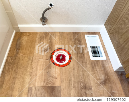 A bathroom under renovation featuring new vinyl flooring and a removed toilet. The base plumbing and toilet paper holder remain, while the area is prepared for the next installation step. 119307602