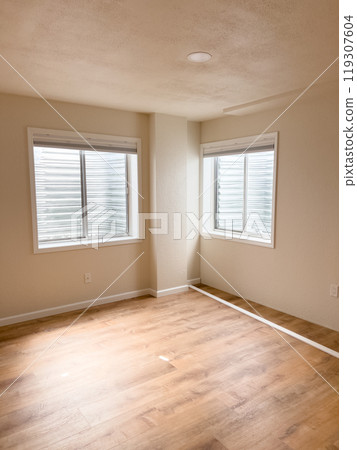 A room with fresh wooden flooring, two windows, and white vinyl baseboards positioned along the walls, ready for installation. The space is bright and shows progress in the renovation process. A room with fresh wooden flooring, two windows, and white vinyl baseboards positioned along the walls, ready for installation. The space is bright and shows progress in the renovation process. 119307604