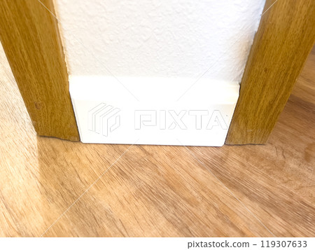 White vinyl baseboards and trim pieces are neatly stacked against a wall, prepared for installation in a room with wooden flooring. The renovation project is in progress, ready to complete the room 119307633