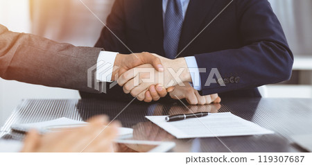 Handshake as successful negotiation ending, close-up. Unknown business people shaking hands after contract signing in modern office 119307687