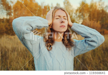 Upset exhausted young woman with headache, pain tension in the head, suffers from migraine outdoors 119308641