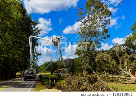 Emergency service linemen are diligently repairing power electrical lines damaged by hurricane using utility tower trucks Emergency service linemen are diligently repairing power electrical lines damaged by hurricane using utility tower trucks 119310961