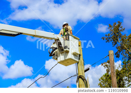 Professional electrician is working on repairing electric power system after Hurricane by using hydraulic tower mounted bucket mounted on truck. 119310998