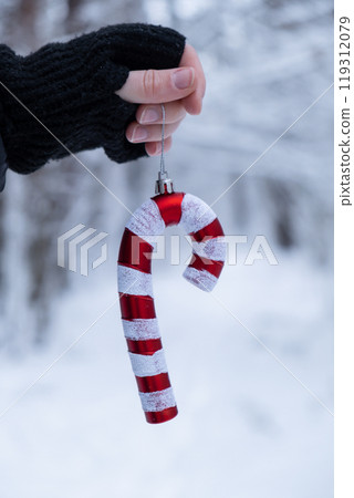 Female hands holding Christmas decoration outdoor in snowy winter forest. Postcard greeting card mock up. Holiday candy toy branch Ornaments Female hands holding Christmas decoration outdoor in snowy winter forest. Postcard greeting card mock up. Holiday candy toy branch Ornaments 119312079