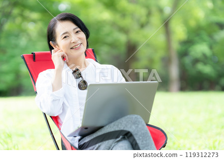 A middle-aged woman working remotely at a campsite A middle-aged woman working remotely at a campsite 119312273