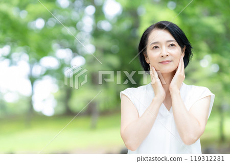 A middle-aged woman doing skin care in the midst of fresh greenery 119312281