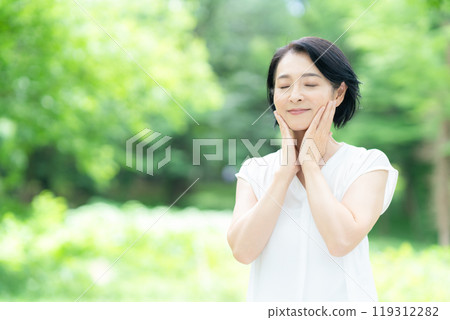 A middle-aged woman doing skin care in the midst of fresh greenery 119312282