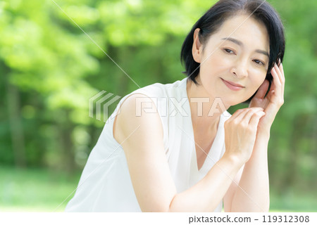 A middle-aged woman doing skin care in the midst of fresh greenery A middle-aged woman doing skin care in the midst of fresh greenery 119312308