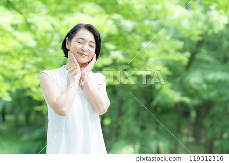 A middle-aged woman doing skin care in the midst of fresh greenery A middle-aged woman doing skin care in the midst of fresh greenery 119312316