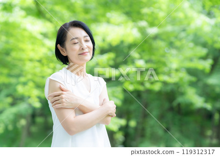 A middle-aged woman doing skin care in the midst of fresh greenery A middle-aged woman doing skin care in the midst of fresh greenery 119312317