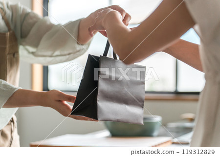 A female cafe attendant handing out takeaway items to customers at a cafe or restaurant 119312829