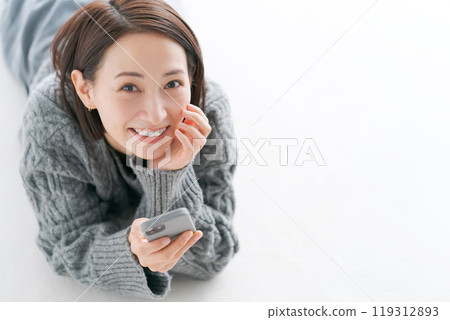 一名婦女躺在地板上操作智慧型手機 一名婦女躺在地板上操作智慧型手機 119312893