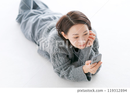一名婦女躺在地板上操作智慧型手機 一名婦女躺在地板上操作智慧型手機 119312894