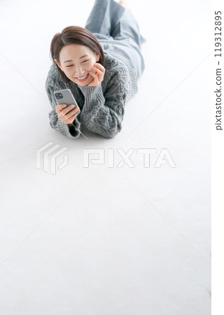 一名婦女躺在地板上操作智慧型手機 一名婦女躺在地板上操作智慧型手機 119312895