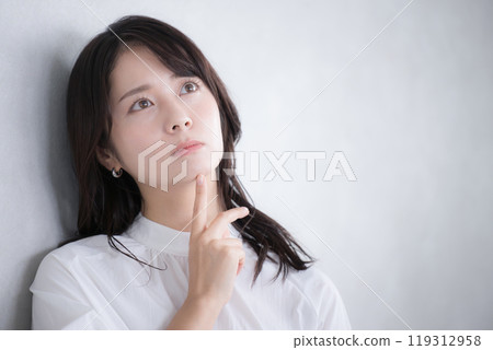 Close-up of a young woman looking up and thinking about changing jobs or quitting her job, gray background 119312958