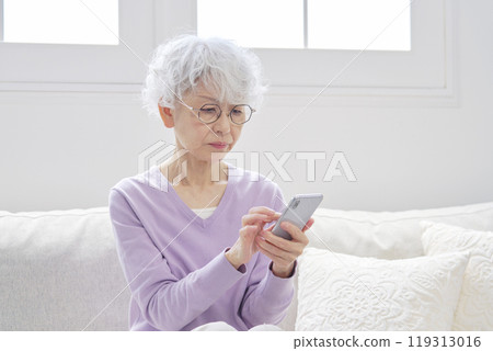 Anxious senior woman using smartphone in living room Anxious senior woman using smartphone in living room 119313016