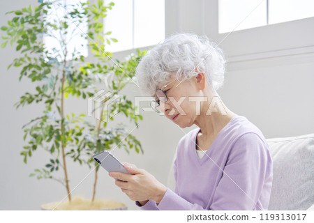 Anxious senior woman using smartphone in living room Anxious senior woman using smartphone in living room 119313017