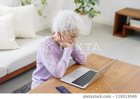 Senior woman feeling depressed while using a laptop in living room 119313049