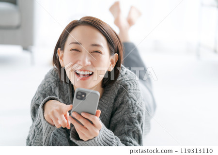 A woman lying on the floor and operating a smartphone 119313110