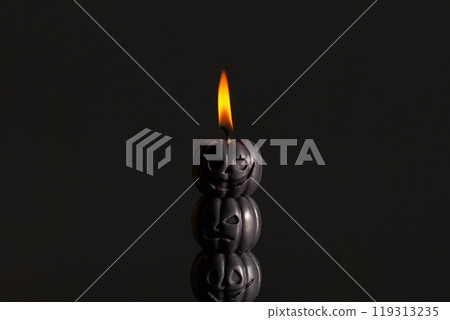Black pumpkin candle burning brightly against dark backdrop, creating a spooky atmosphere 119313235