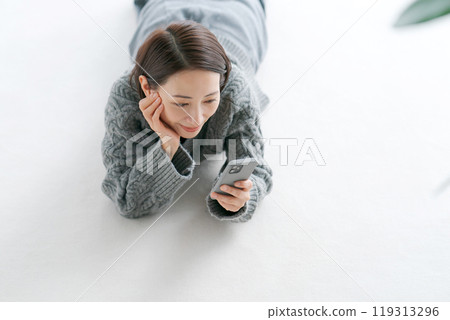 一名婦女躺在地板上操作智慧型手機 119313296