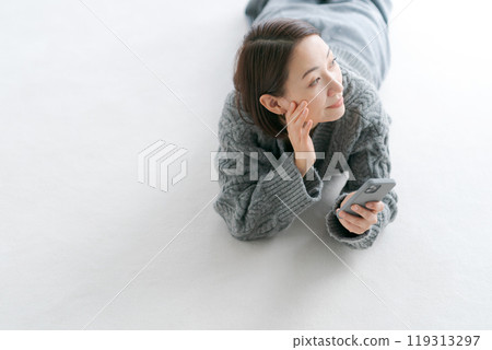 一名婦女躺在地板上操作智慧型手機 一名婦女躺在地板上操作智慧型手機 119313297