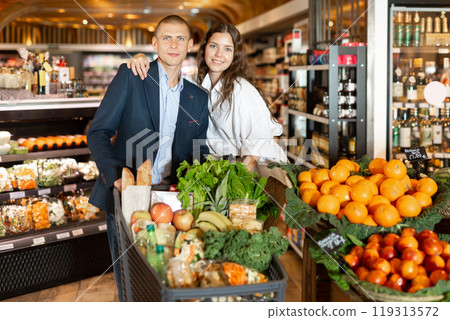 Portrait of a happy young couple with products in a cart in the supermarket Portrait of a happy young couple with products in a cart in the supermarket 119313572