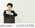 20 多歲的日本男子穿著西裝坐在椅子上，看著他的智慧型手機 119313708