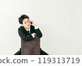 20 多歲的日本男子穿著西裝坐在椅子上打電話 119313719