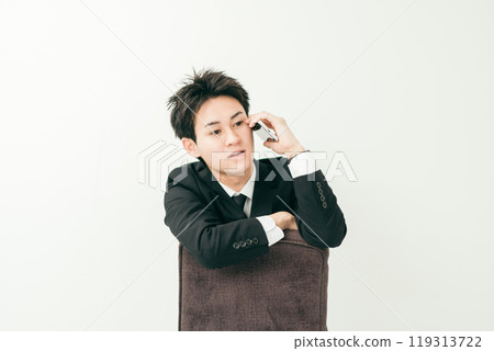 20 多歲的日本男子穿著西裝坐在椅子上打電話 119313722