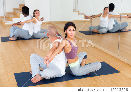 Women and men exercising in pairs during yoga class in fitness center Women and men exercising in pairs during yoga class in fitness center 119313828