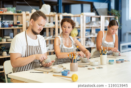 Three pottery students mold clay into homemade plates and other utensils 119313945