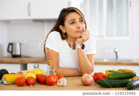 Frustrated young Hispanic woman standing in home kitchen 119313993