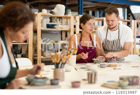 During master class, student paints clay vessel under guidance of male teacher. 119313997