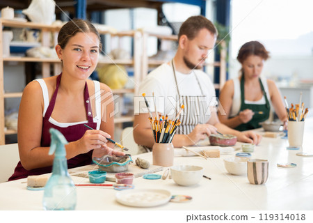 Pottery workers paint ceramic plates together at table Pottery workers paint ceramic plates together at table 119314018